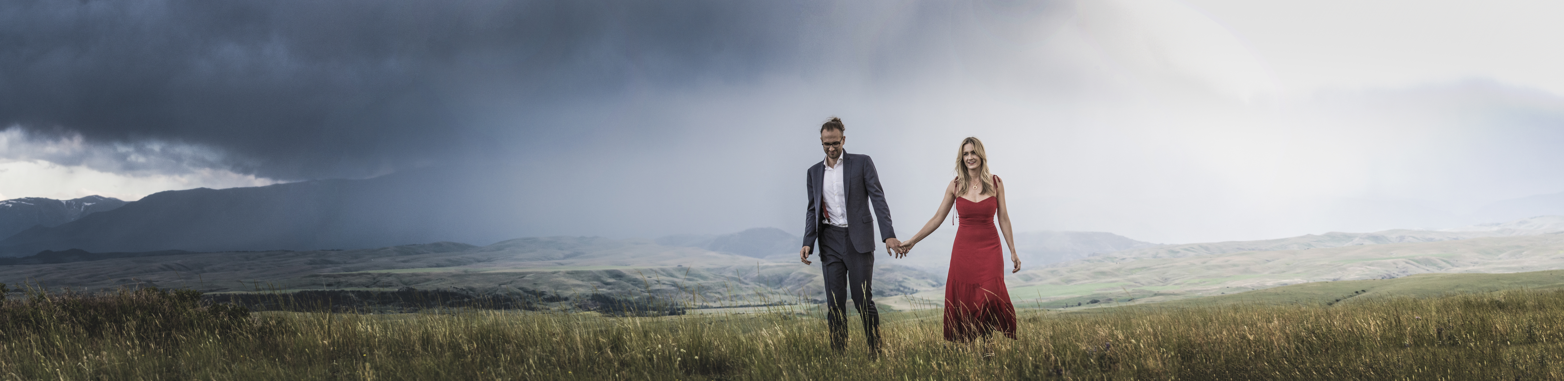 A couple standing small on an alpine ridge at dusk in vast mountain wilderness